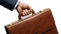 Close-up of male hand holding brown leather briefcase against white background. Professional businessman carrying work bag for corporate business, finance, and career concepts.