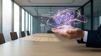 Businessman hand presenting holographic gear mechanism with glowing connections in modern conference room for technology innovation concepts.