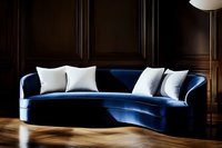 Curved navy blue velvet sofa with white throw pillows against dark wood paneled wall, luxurious living room interior with herringbone hardwood flooring.