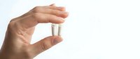 Hand holding clear glass vial or test tube between fingers against white background. Laboratory sample container for medical research and scientific testing.