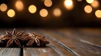 Star anise spice on rustic wooden table with blurred golden bokeh lights in background creating cozy festive atmosphere for holiday baking and cooking.