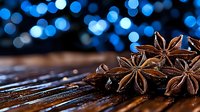 Star anise pods on rustic wooden surface with blue bokeh lights in background creating magical festive atmosphere for winter holiday season cooking.