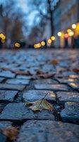 Fallen autumn leaf on wet cobblestone street at dusk with bokeh lights creating magical evening atmosphere, shallow depth of field captures urban romance.