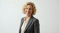 Professional mature blonde businesswoman in gray suit smiling confidently against white background for corporate presentations and marketing materials.