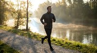 Athletic man jogging along misty river path during golden hour sunrise workout in peaceful natural setting for fitness and wellness lifestyle content.