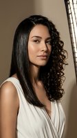 Young Hispanic woman with straight and curly mixed hairstyle in white wrap top by window with natural lighting for beauty and fashion concepts.