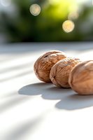 Fresh whole walnuts casting shadows on white surface with soft natural light and bokeh effect in background, minimalist food composition for healthy eating concept.