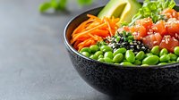 Fresh poke bowl with raw salmon, edamame beans, carrots, avocado and sesame seeds in black ceramic bowl on dark background. Healthy food concept.