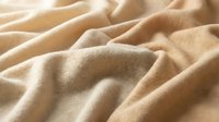 Beige linen fabric with soft folds and natural texture, suitable for home decor, fashion design, and textile backgrounds.