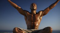 Athletic Black man with muscular torso meditating at sunset, arms outstretched in freedom pose against blue sky background, expressing wellness and spiritual balance.