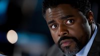 Young African American businessman with beard in dark suit looking concerned against blurred night city background with bokeh lights, dramatic portrait.