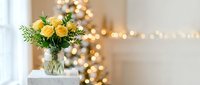 Yellow roses in glass vase on white table with warm bokeh lights creating cozy home atmosphere for holiday celebrations and interior design.