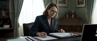 Professional middle-aged Caucasian businesswoman with glasses working at desk in elegant home office, reviewing documents with laptop open for remote work.
