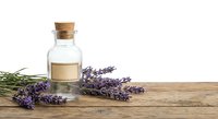 Lavender essential oil bottle with cork stopper and fresh purple lavender flowers on rustic wooden surface for aromatherapy and natural wellness products.
