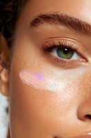 Close-up of green eye with holographic highlighter makeup on tanned skin with freckles, showing modern beauty trends and glowing complexion.