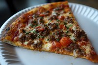 Fresh slice of pizza with seasoned ground beef, melted mozzarella cheese, diced tomatoes and herbs served on white paper plate, close up view of Italian cuisine.