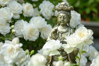 Peaceful bronze Buddha statue surrounded by blooming white roses in serene garden setting for meditation and spiritual wellness concepts.