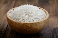 White jasmine rice grains in bamboo bowl on rustic wooden table background, close up view of raw uncooked rice for Asian cuisine and cooking.