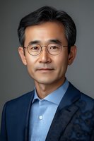 Professional headshot of middle-aged Asian businessman wearing navy suit, light blue checkered shirt and round glasses against grey background. Confident executive portrait.