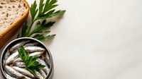 Canned anchovies in oil with fresh parsley and sliced bread on white background, suitable for food styling and culinary content.