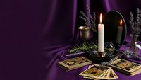 Mystical tarot card reading setup with burning candle, crystal ball and lavender on purple silk fabric for fortune telling and divination practices.