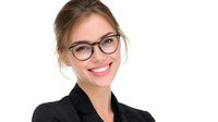 Young Caucasian businesswoman wearing glasses and black blazer smiling confidently at camera. Professional corporate headshot with natural lighting and white background.