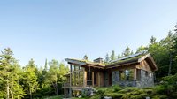 Modern luxury cabin with stone and wood exterior nestled in forest setting with large windows and contemporary architecture for vacation rental marketing.