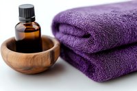 Essential oil in wooden bowl next to folded purple spa towels on white background, wellness and aromatherapy concept for massage and relaxation treatments.