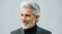 Senior man with gray hair and beard wearing dark turtleneck and blazer, smiling confidently against neutral background. Suitable for business, lifestyle, and professional portraits.