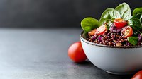 Fresh black rice bowl with cherry tomatoes and green spinach leaves on gray concrete background, healthy vegetarian lunch with copy space.