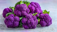 Fresh purple cauliflower heads with green leaves on light background, organic farming produce for healthy eating and natural food photography.