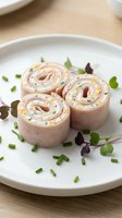 Sliced turkey and cream cheese pinwheels arranged on white plate with fresh microgreens and chives, ideal for appetizers, catering, and food styling.