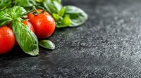 Fresh ripe tomatoes and aromatic basil leaves on dark stone background with water drops and copy space for menu or recipe design.