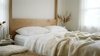 Cozy unmade bed with white linen bedding and wooden headboard in bright minimalist bedroom interior for home decor and lifestyle concepts.