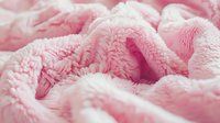 Soft pink plush blanket texture with gentle folds and waves creating cozy comfortable background pattern for feminine designs and warm lifestyle concepts.