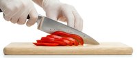 Chef in gloves slicing fresh red bell pepper on wooden cutting board with sharp knife, isolated on white background.