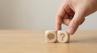 Hand placing wooden cube with question mark next to speech bubble block on desk for business communication and problem solving concepts.
