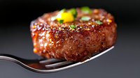 Juicy grilled beef steak on fork with herbs and spices against dark background, close up macro shot showing meat texture and caramelized crust.