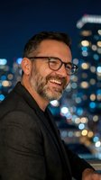 Smiling middle-aged Caucasian businessman with glasses and beard against blurred city lights at night for corporate headshots and professional marketing.