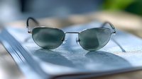 Stylish metal frame sunglasses with dark lenses placed on open book pages with shallow depth of field creating soft blurred background effect.