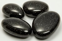 Polished black obsidian stones with sparkling inclusions arranged on white background, showing smooth surface texture and natural mineral formations for healing practices.