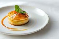 Elegant lemon tart with caramelized sugar spiral and fresh mint garnish on white plate. Gourmet dessert presentation for fine dining and culinary arts.