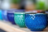 Colorful ceramic teacups with geometric patterns in blue and turquoise tones arranged in row on wooden surface, shallow depth of field creates artistic blur effect.
