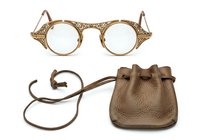 Ornate round eyeglasses with decorative gold filigree frames and small brown leather drawstring pouch isolated on white background, ready for fashion and accessory design use.