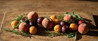Fresh stone fruits and herbs arranged on rustic wooden cutting board for culinary photography and food styling projects.
