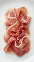 Thinly sliced prosciutto ham arranged on white background, cured meat delicatessen product for gourmet cooking and charcuterie boards.