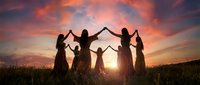 Group of women holding hands in circle formation silhouetted against dramatic sunset sky in open field creating unity and connection concept.