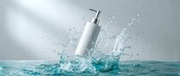 White cosmetic bottle with pump dispenser splashing into clear turquoise water creating dynamic splash effect on clean background for skincare advertising.