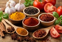 Colorful spices in wooden bowls with fresh vegetables, garlic, tomatoes and herbs on rustic wood background for cooking and culinary recipes.