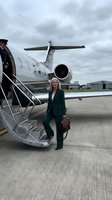 Middle-aged Caucasian businesswoman in dark green blazer exiting private jet with leather briefcase. Corporate travel and executive lifestyle concept.